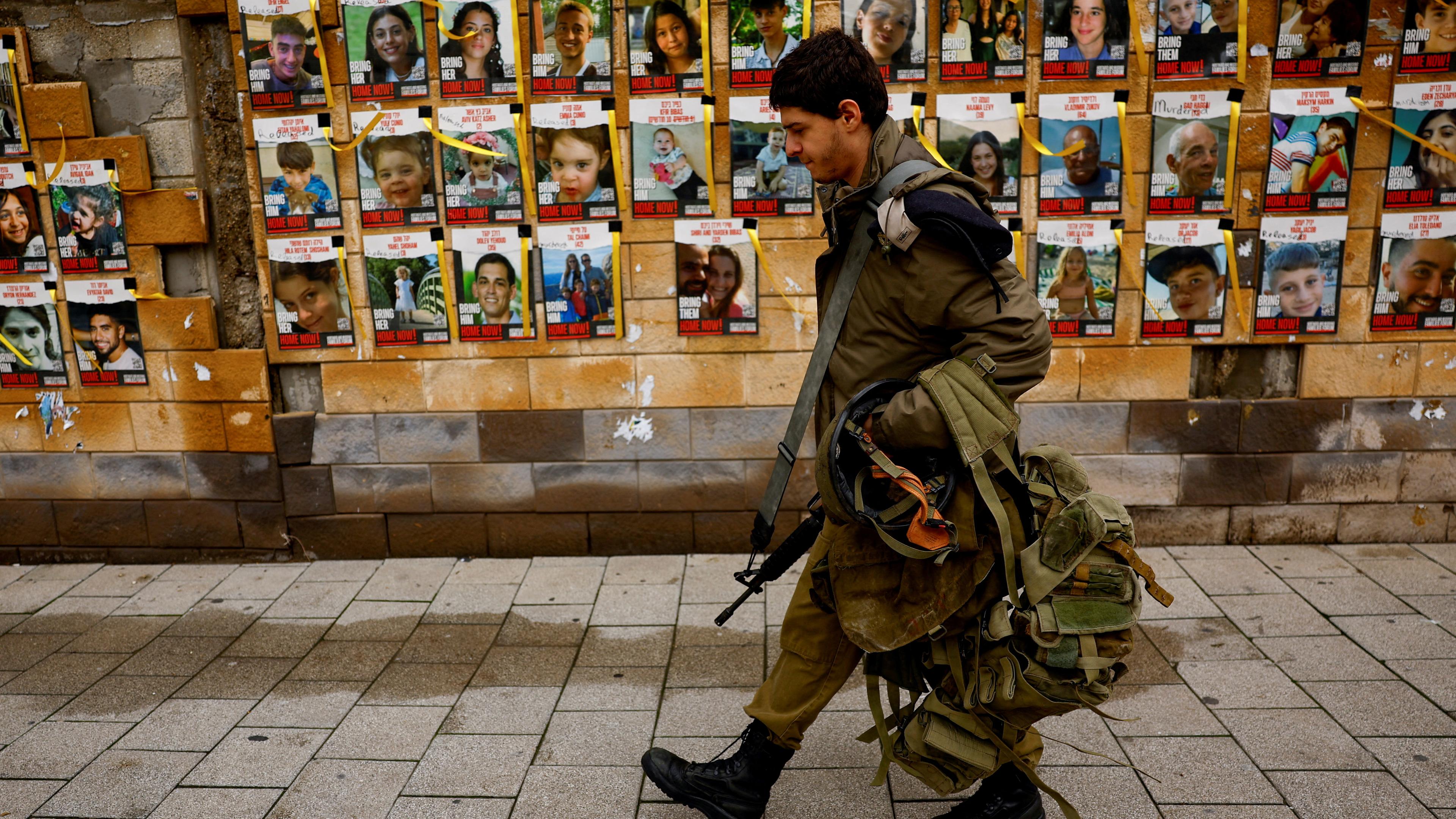 Ein israelischer SOldat läuft an einer Wand vorbei, an der mehrere Plakate mit Bilder der verschleppten Geiseln befässtigt sind.