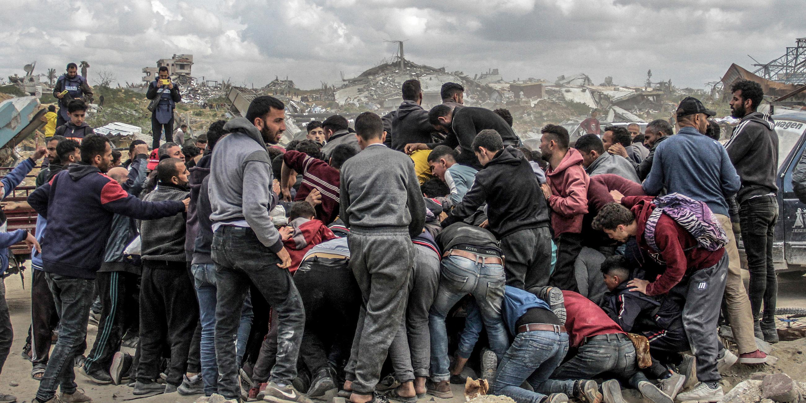 Menschen drängen sich um Pakete mit humanitärer Hilfe, die über dem nördlichen Gazastreifen abgeworfen wurden, aufgenommen am 25.03.2024