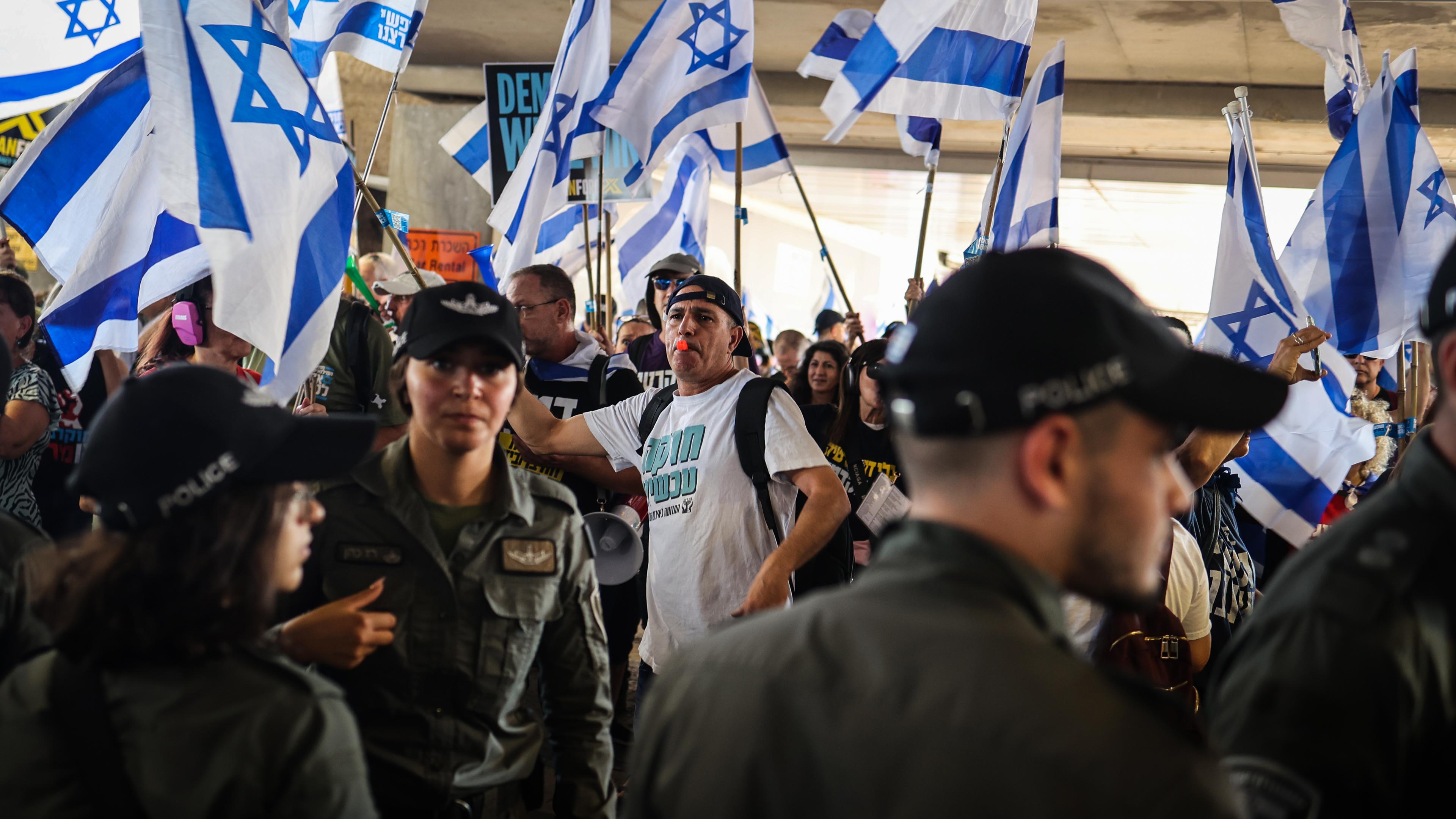 Zu sehen sind Protestierende und israelische Polizisten; im Hintergrund Israel-Flaggen.