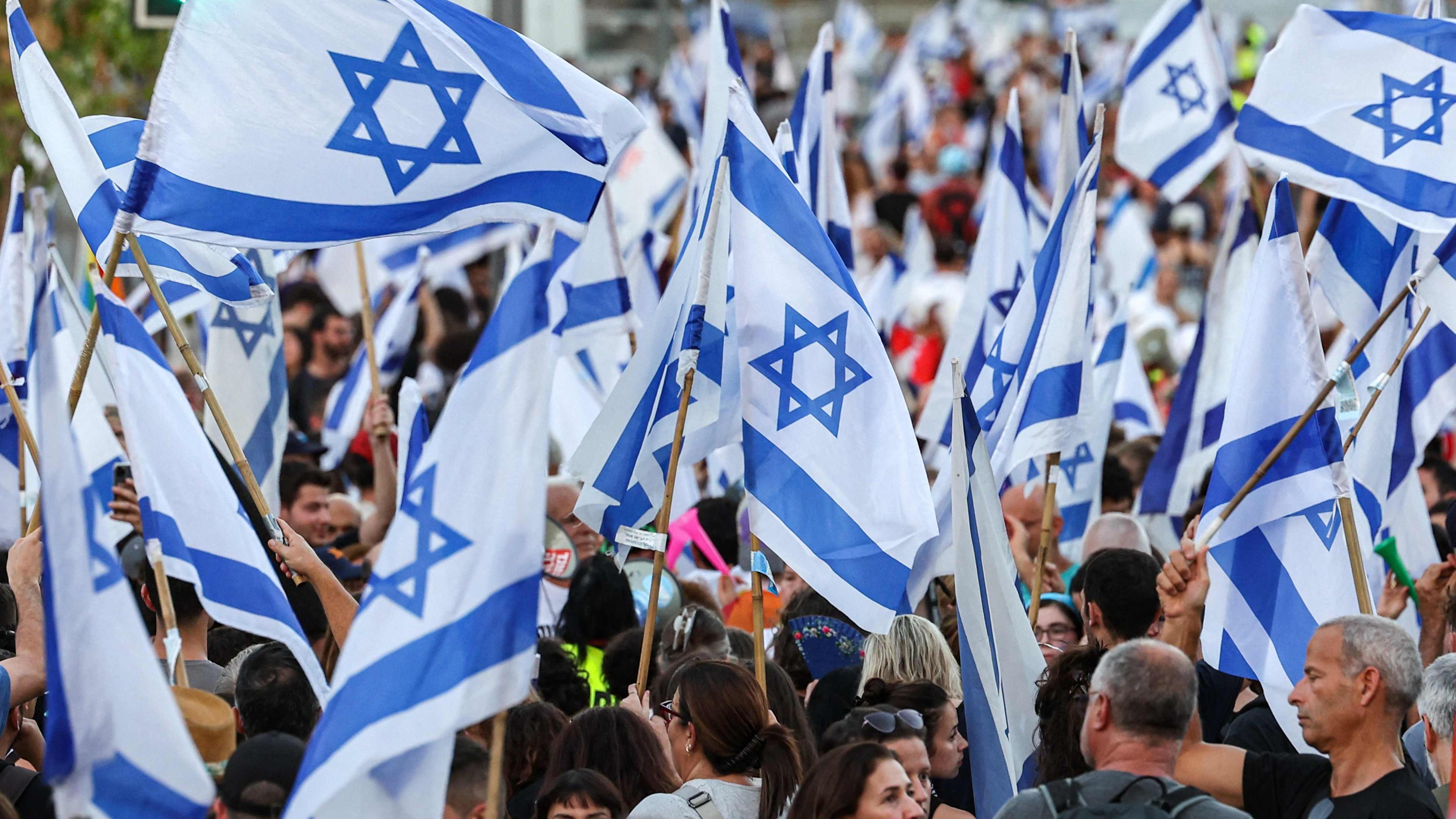 Menschen protestieren auf der Straße und halten israelische Flaggen in der Hand.
