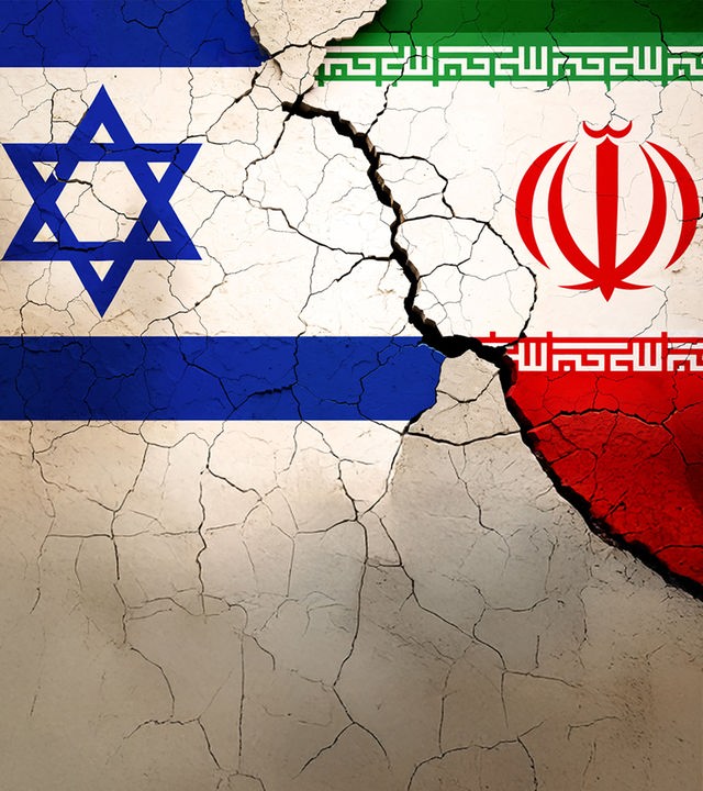 Die Flaggen von Israel (links) und Iran (rechts) nebeneinander auf einer Mauer mit vielen Rissen