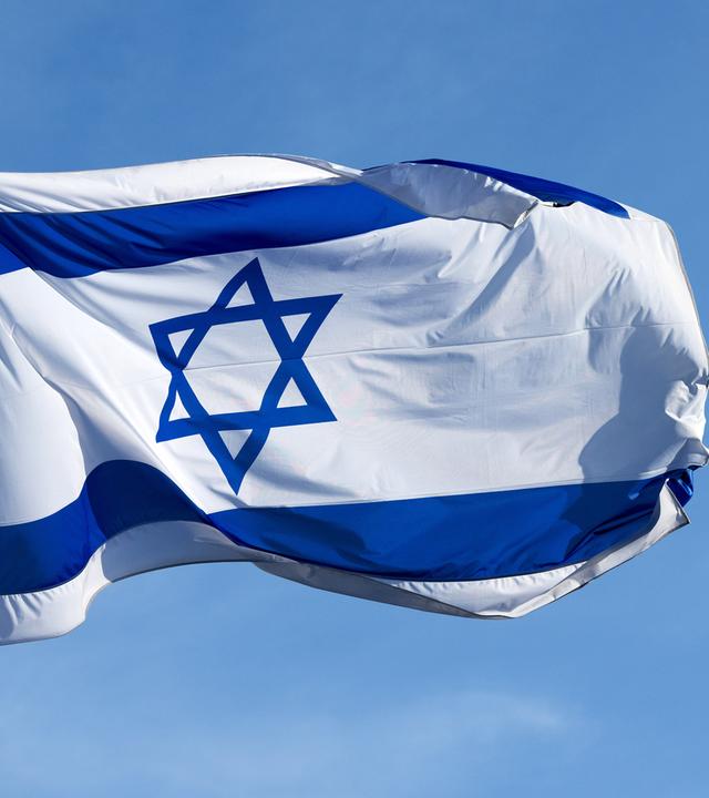 Die israelische Flagge - ein blauer sechseckiger Stern auf weißem Grund zwischen zwei blauen Balken - weht vor blauem Himmel.