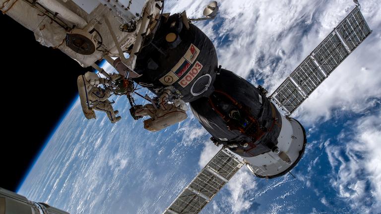 Auf dem bild sihet man zwei Kosmonauten, die ein Leck an der ISS überprüfen. Im Hintergrund sieht man einen Teil der Erde.