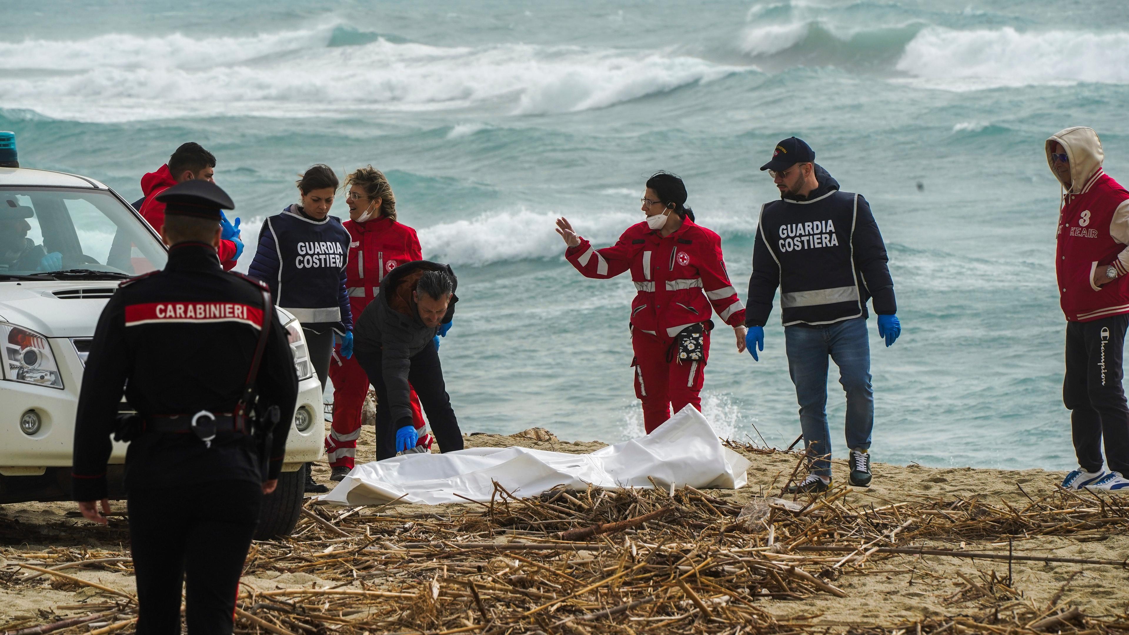 Mitarbeitende des italienischen Roten Kreuzes stehen am Strand und decken eine Leiche ab