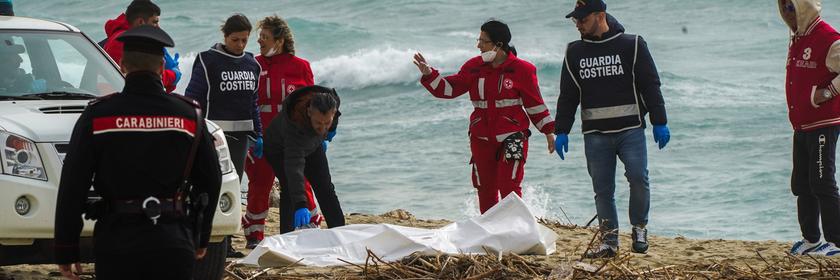 Mitarbeitende des italienischen Roten Kreuzes stehen am Strand und decken eine Leiche ab