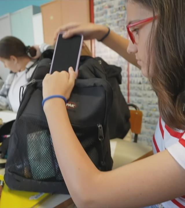 Schülerin, die ihr Handy für den Unterricht in den Rucksack steckt