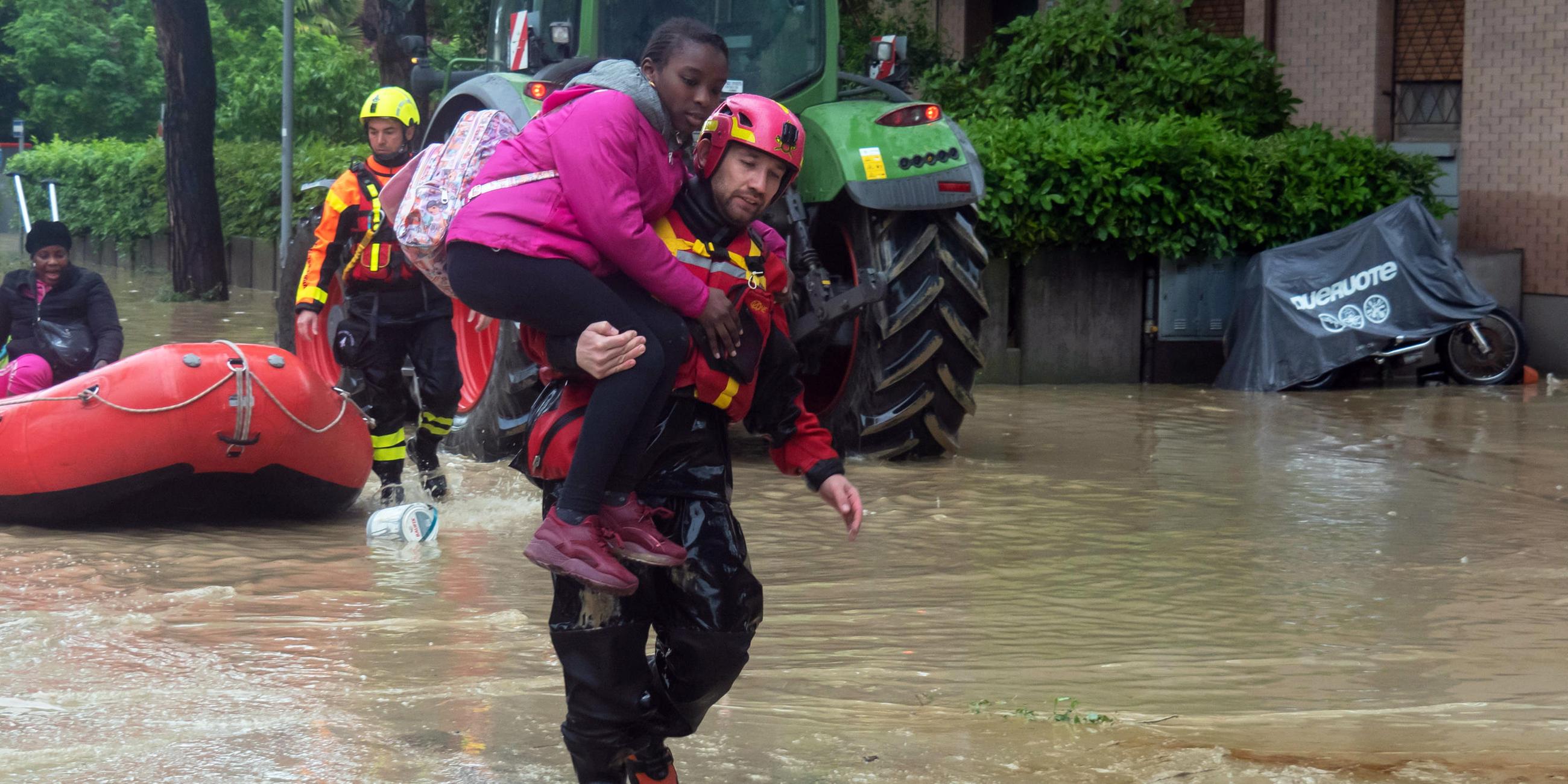Ein Feuerwehrmann trägt ein Mädchen durch überflutete Straßen