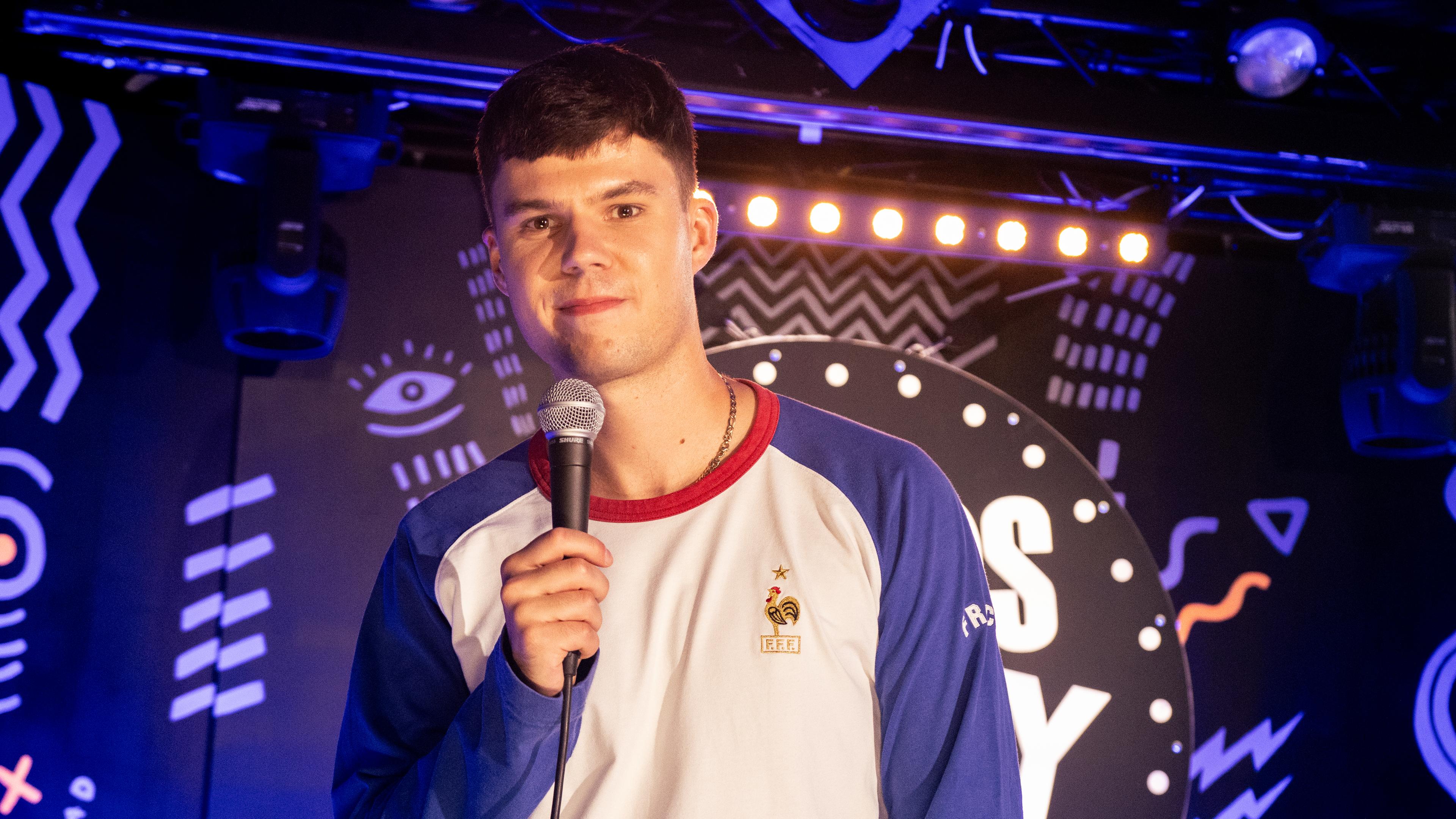 Ivan Thieme steht auf einer Bühne. Der Hintergrund ist blau beleuchtet. 