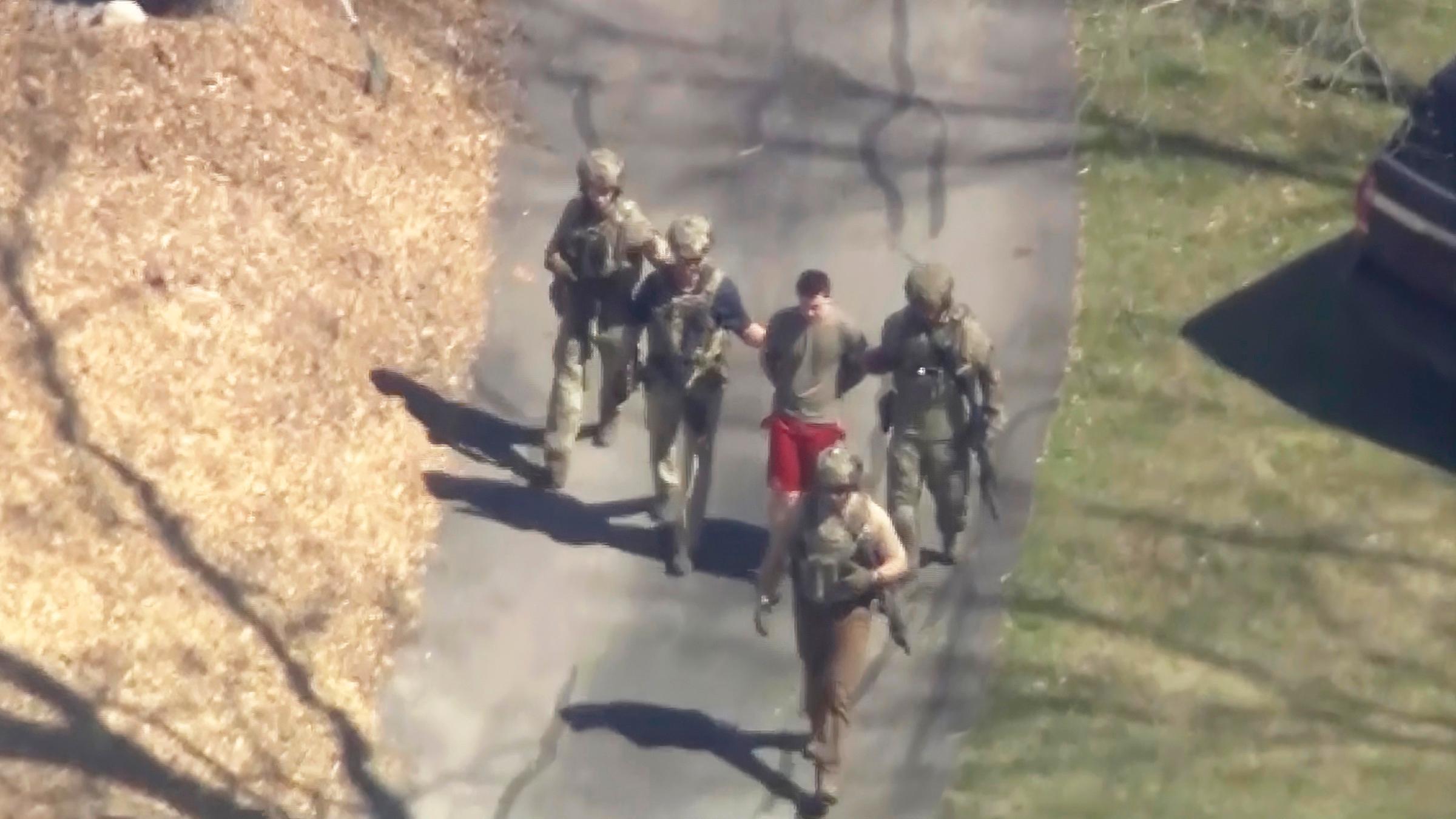 Jack T. in T-Shirt und Shorts, der von bewaffneten Einsatzkräften in Gewahrsam genommen wird