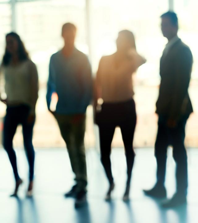 Zwei Frauen und zwei Männer stehen nebeneinander in einem Raum. Man erkennt nur ihre Umrisse. Im Hintergrund eine Fensterfront.