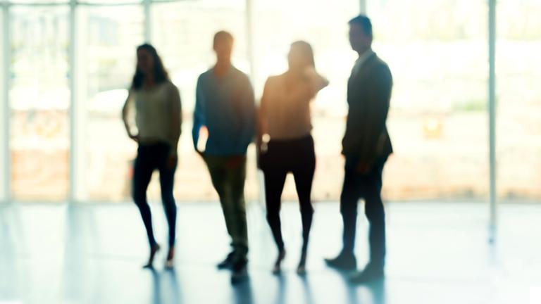 Zwei Frauen und zwei Männer stehen nebeneinander in einem Raum. Man erkennt nur ihre Umrisse. Im Hintergrund eine Fensterfront.