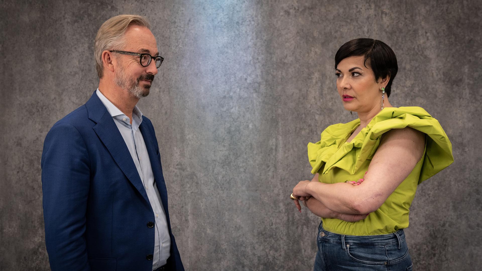 Jan Fleischhauer und Reyhan Şahin stehen vor einer grauen Wand und beäugen sich kritisch