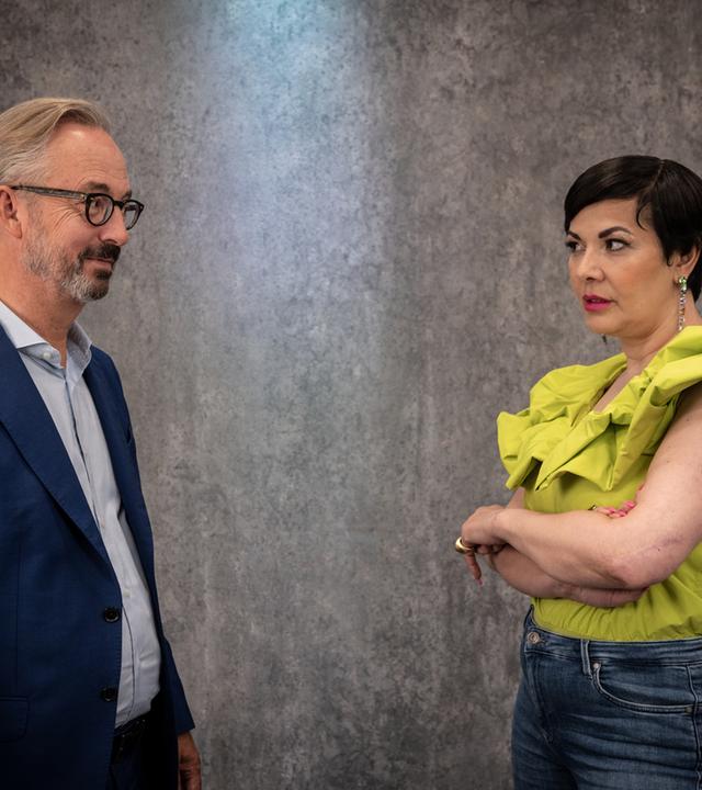 Jan Fleischhauer und Reyhan Şahin stehen vor einer grauen Wand und beäugen sich kritisch