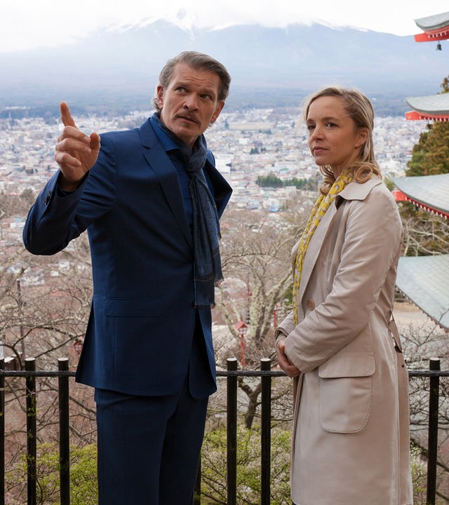 "Das Traumschiff: Japan": Saskia (Johanna Klante) und Hendrik Claasen (Götz Otto) stehen oberhalb einer Stadt. Hendrik zeigt mit dem Finger auf etwas und beide blicken in die Ferne. Im Hintergrund ist ein japanischer Tempel zu sehen.