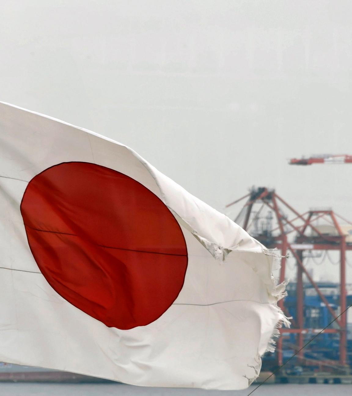die japanische Flagge weht im Wind, im Hintergrund ist ein großer Hafenkrahn im Hafen Tokios