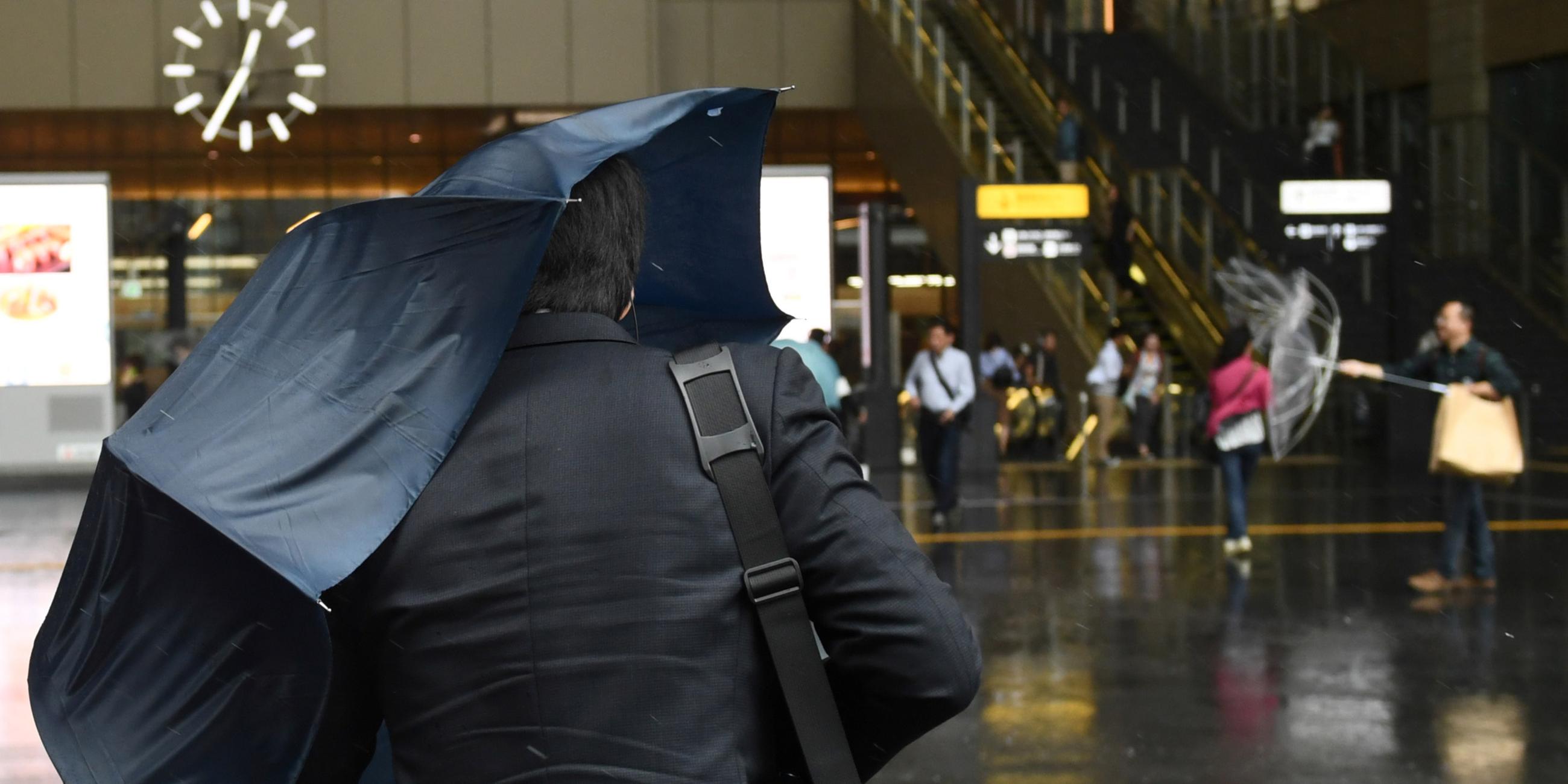 Passanten in Osaka kämpfen im Unwetter mit ihren Regenschirmen.