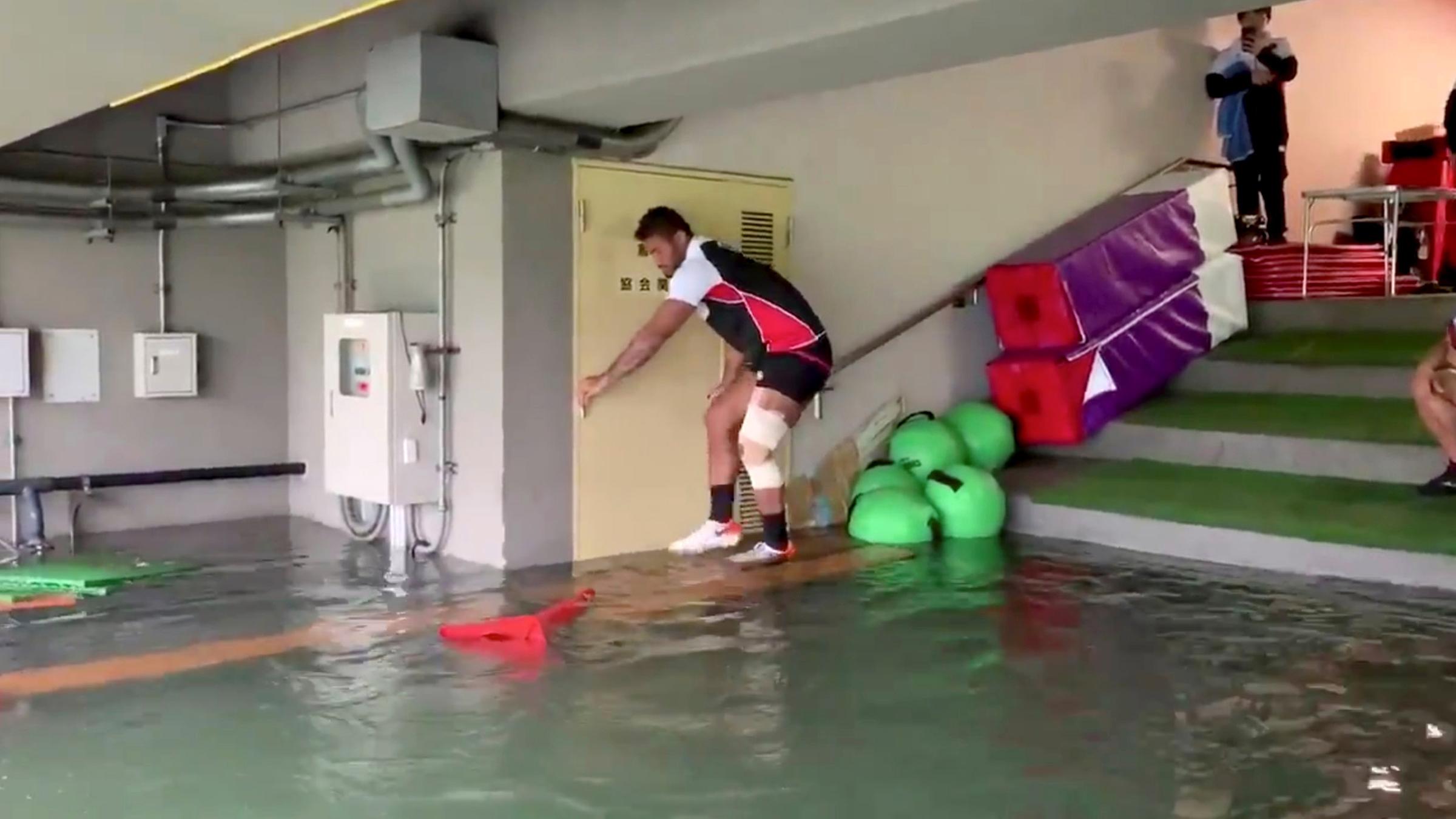 Ein Spieler des japanischen Rugby-Teams klettert über Tische, um trocken durch einen überfluteten Kabinengang zu kommen.