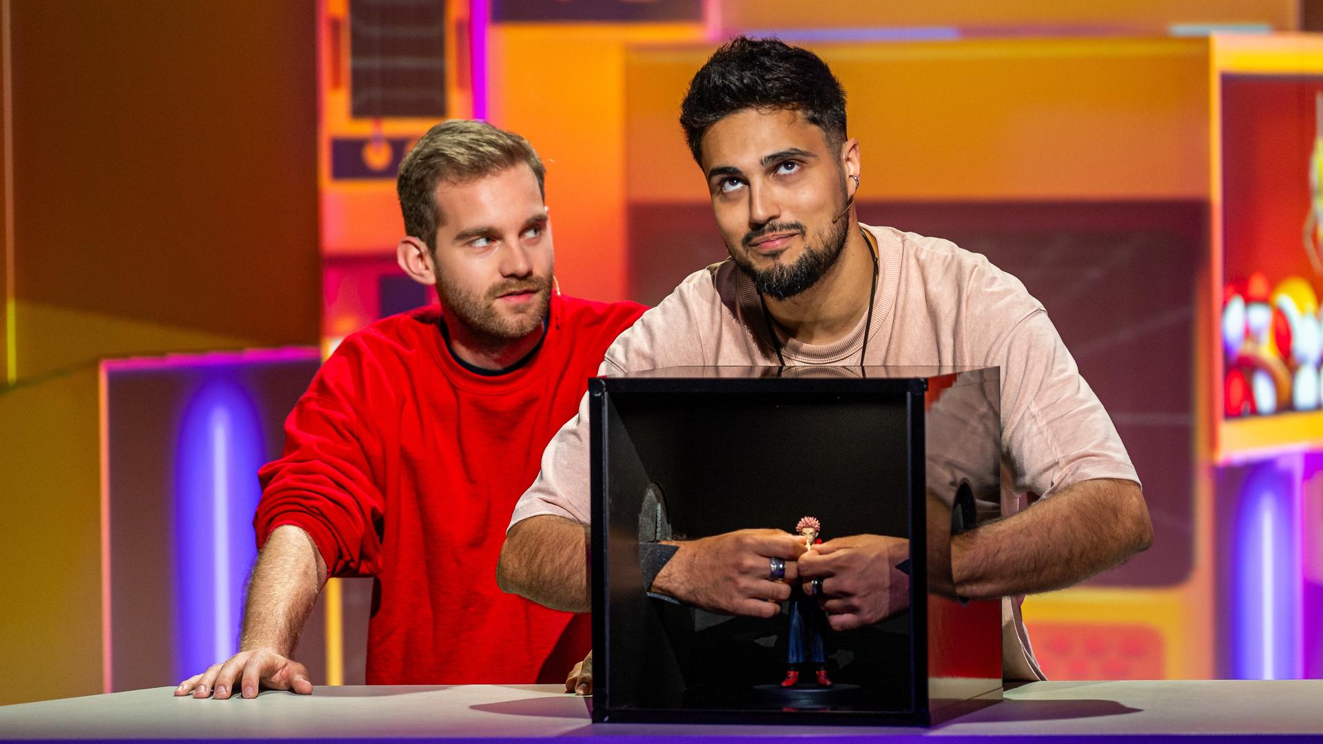 Tanoshii: Jaydred und Ihabo stehen im Tanoshii-Studio am Spielepult. Ihabo ertastet mit den Fingern eine Manga-Franchise-Figur.