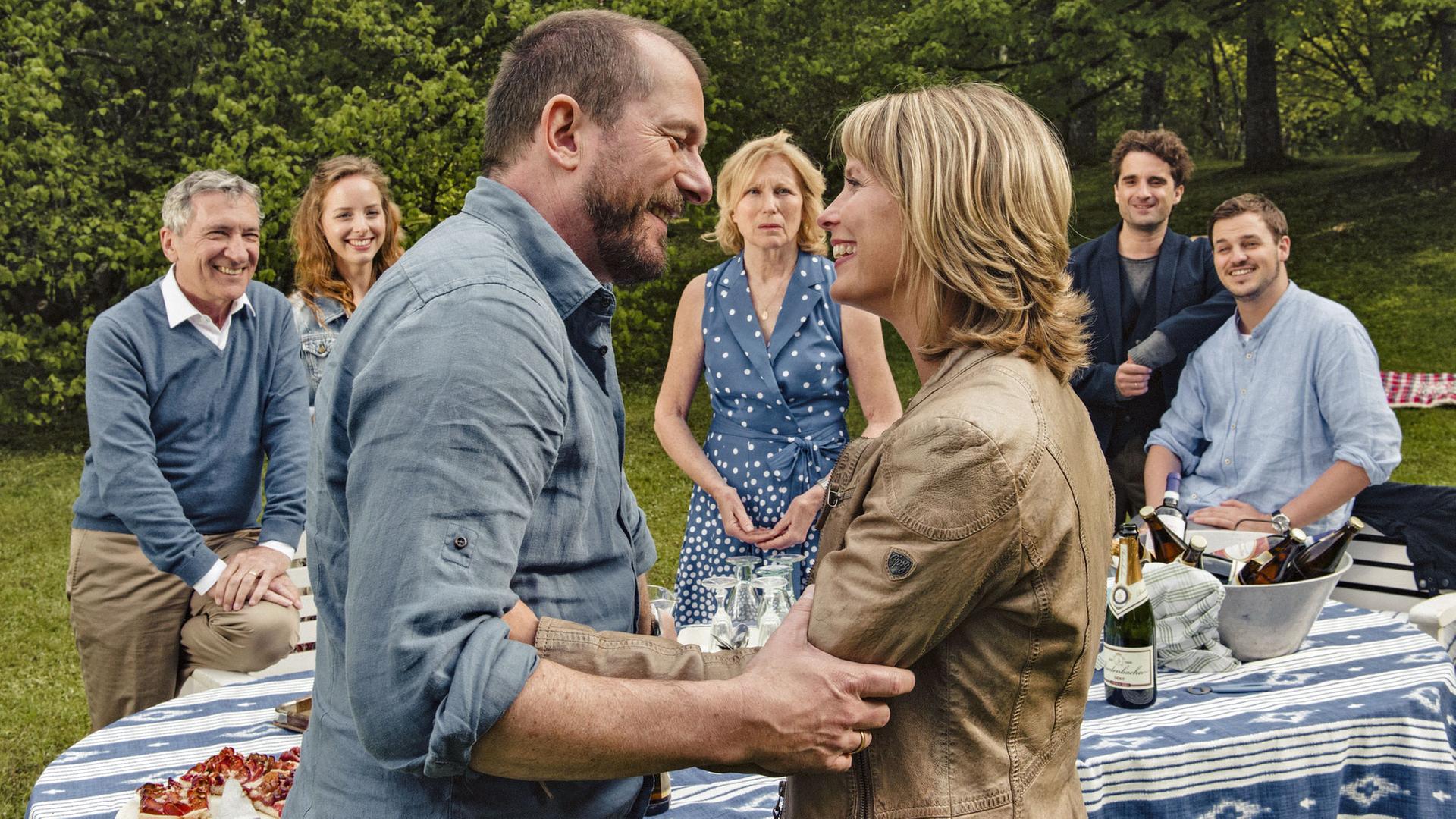 "Jella jagt das Glück": Hilke (Valerie Niehaus) und Franz (Martin Lindow) stehen sich vorm Gartentisch gegenüber, halten sich an beiden Armen fest. Jella (Maren Kroymann) hinterm Gartentisch mit Klaus (Rudolf Kowalski), Fine (Amelie Plaas-Link), Momme (Oliver Wnuk) und Rudi (Frederic Linkemann).