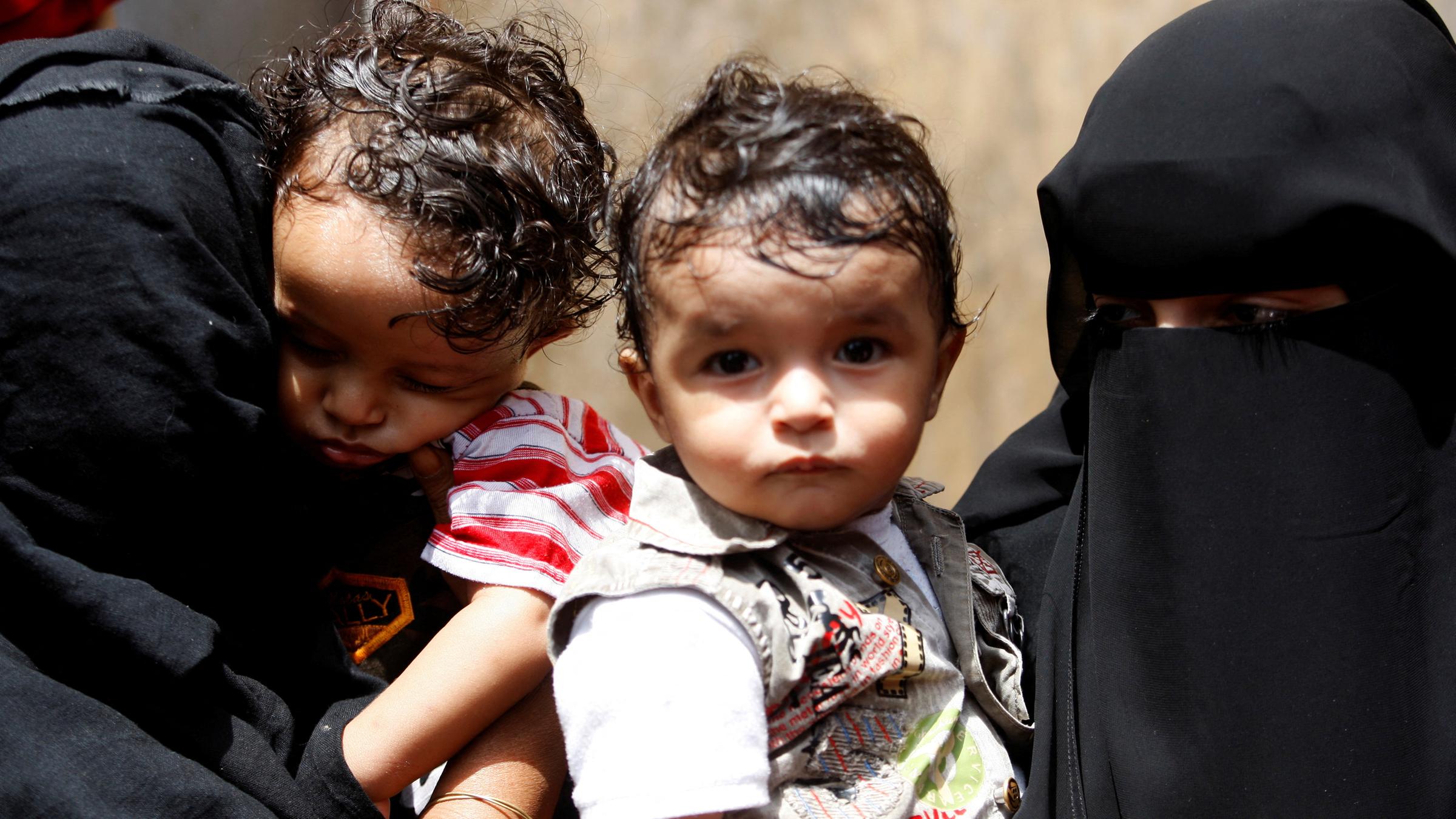 Es sind zwei Frauen in Burkas zu sehen und sie halten ihre kleinen Kindern.