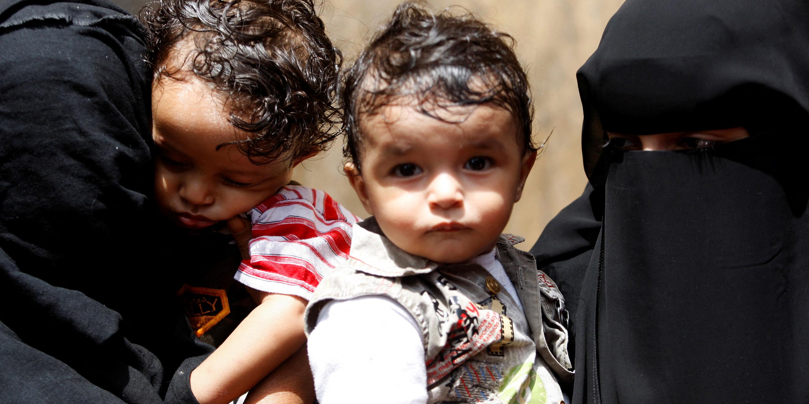 Es sind zwei Frauen in Burkas zu sehen und sie halten ihre kleinen Kindern.