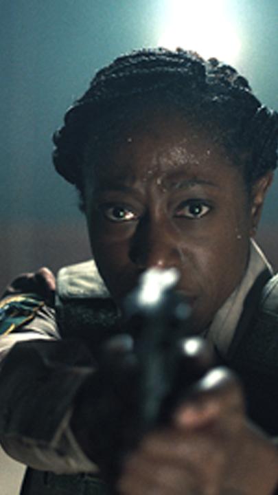 Großaufnahme: Tabby (Nikki Amuka-Bird) zielt mit einer Pistole in Richtung der Kamera.