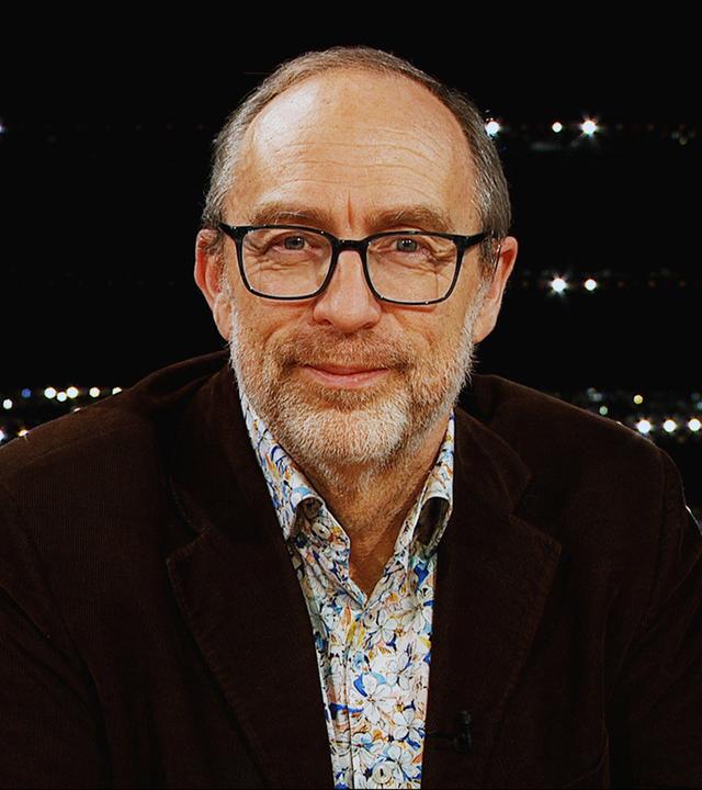 Ein Mann mit Brille schaut vor dunklem Hintergrund in die Kamera