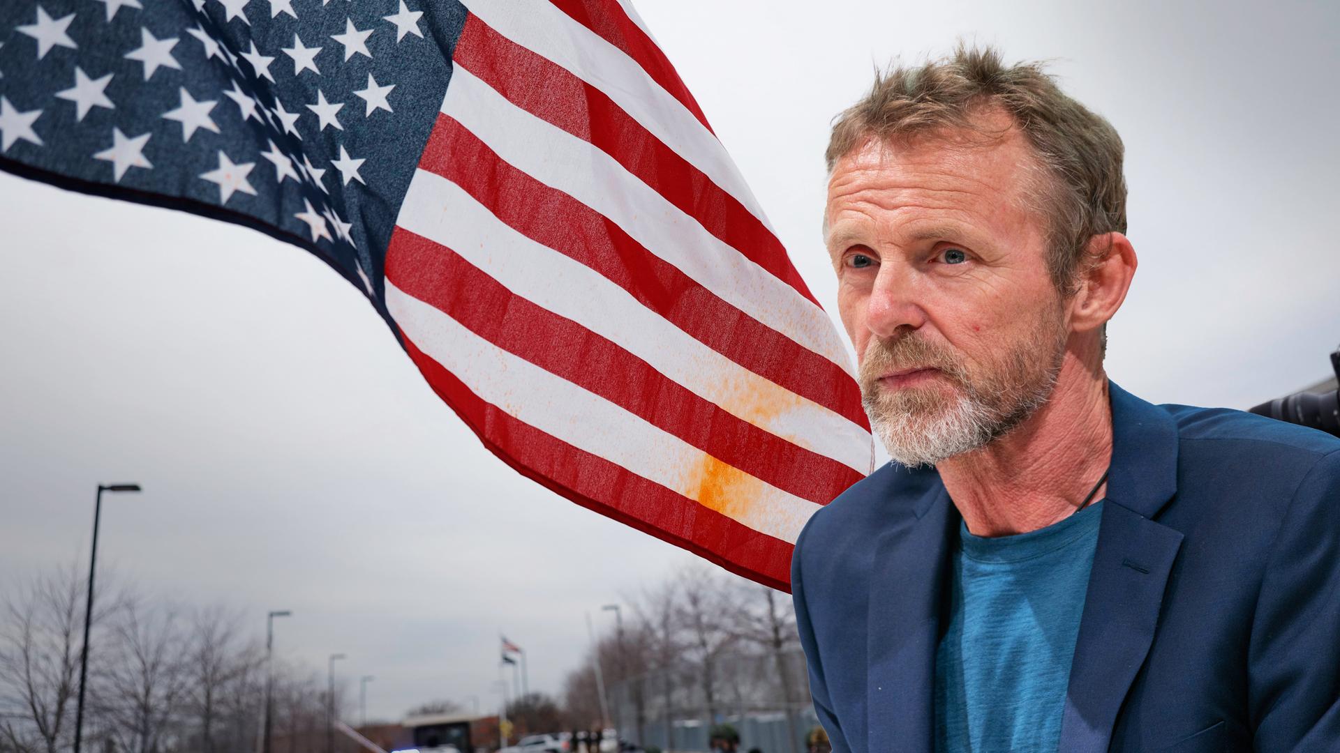 Ein Mann mittleren Alters mit graumeliertem Bart und kurzen Haaren ist vor ein Foto von einer US-Flagge bei einer Demonstration in Minneapolis montiert.