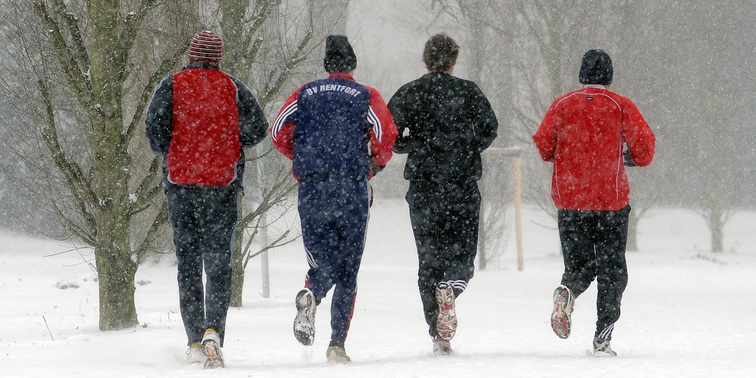 Vier Männer joggen nebeneinander über einen verschneiten Weg.