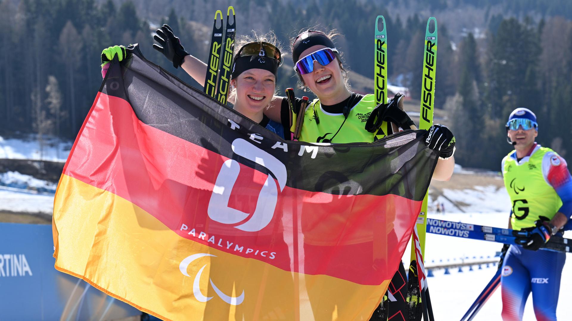 Die sehbehinderte deutsche Biathletin Johanna Recktenwald und ihr Guide Emily Weiss zeigen strahlend die Flagge des deutsche Paralympics Team