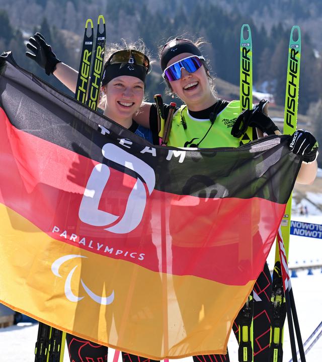 Die sehbehinderte deutsche Biathletin Johanna Recktenwald und ihr Guide Emily Weiss zeigen strahlend die Flagge des deutsche Paralympics Team