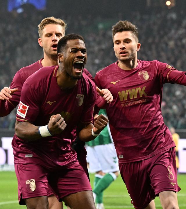 Die Augsburger Arne Maier (l) und Elvis Rexhbecaj (r) jubeln mit dem Torschützen Samuel Essende zum 0:1. 