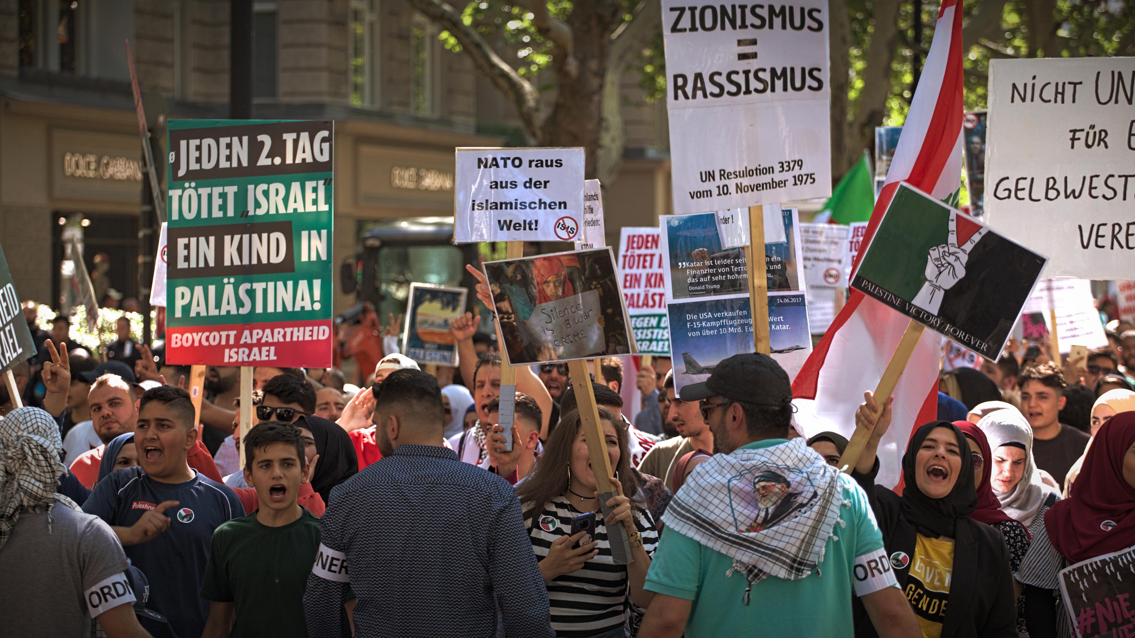 Während einer Demonstration halten mehrere Menschen Schilder in die Luft und schreien. Auf einem der Schilder steht die Aufschrift "Jeden 2. Tag tötet Israel ein Kind in Palästina".