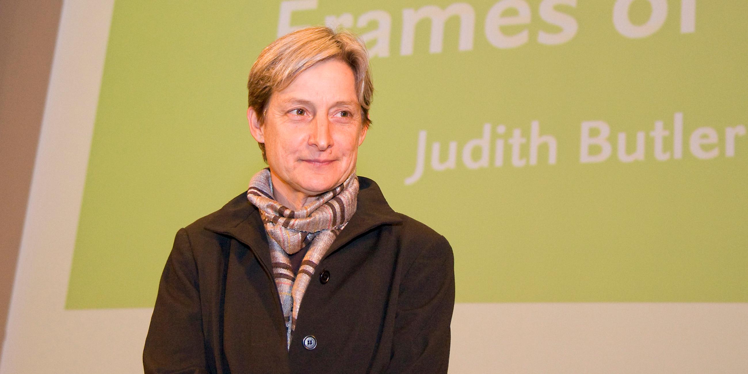 Judith Butler steht vor einem grünen Hintergrund