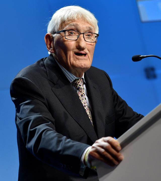 Ein Mann steht vor blauem Hintergrund an einem Rednerpult