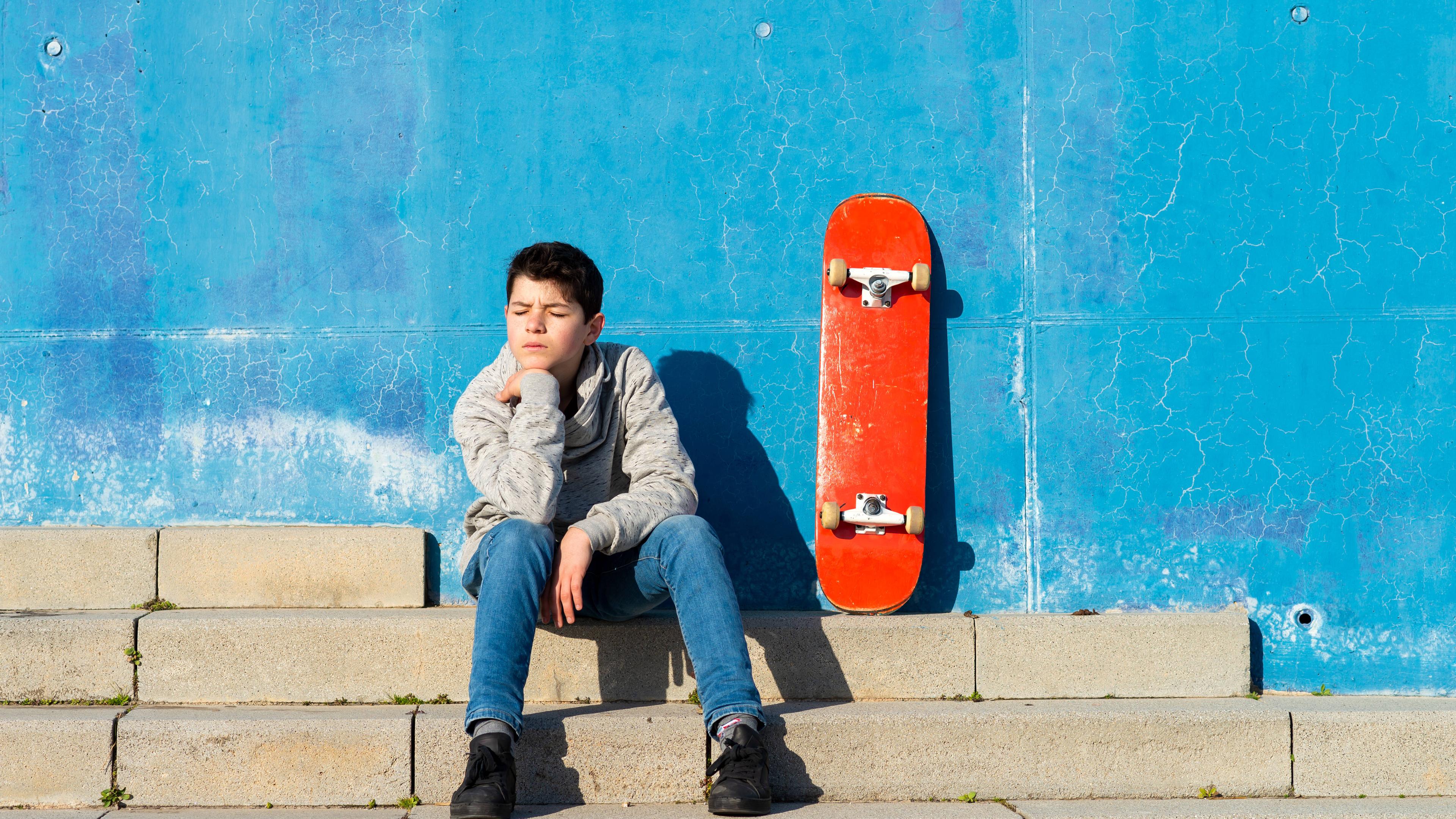 Jugendlicher sitzt traurig an der Wand.