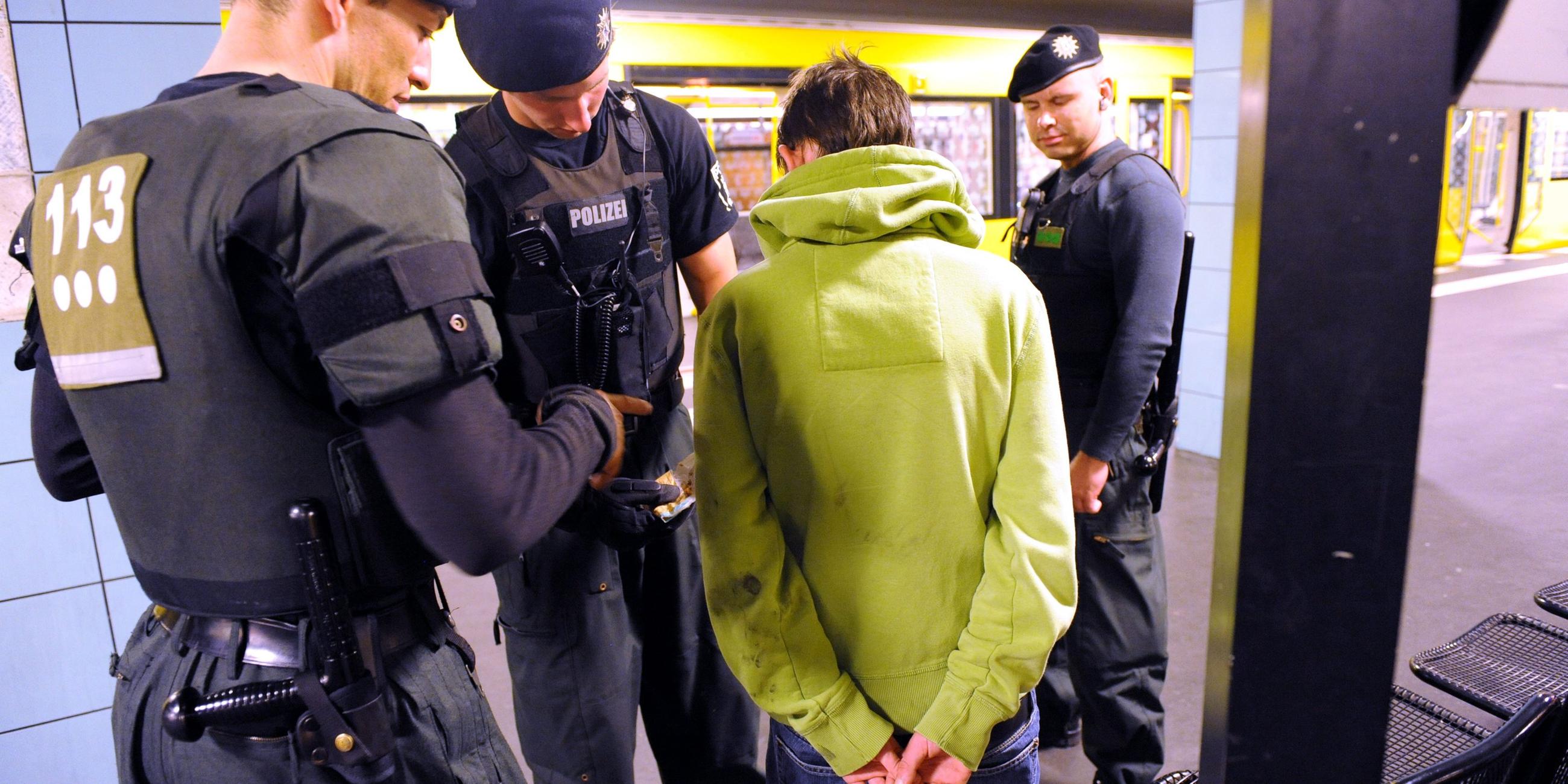 Ein Jugendlicher in grünem Pulli steht in einer U-Bahn-Haltestelle mit dem Rücken zur Kamera. Um ihn herum stehen drei Polizisten.