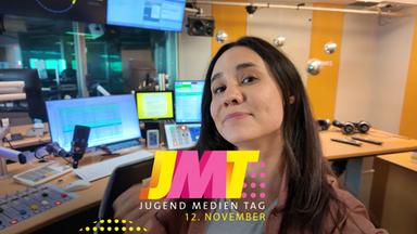 Die Journalistin LEO steht in einem Schneideraum vor mehreren Monitoren, einem Mikrofon und einem Mischpult. Im Vordergrund wirbt ein farbenfroher Schriftzug für den gemeinsamen Jugendmedientag 2026 von ZDF, ARD und Deutschlandfunk am 12. November