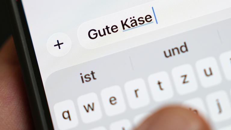 Die Wörter Gute Käse sind auf dem Display eines Smartphones zu lesen.