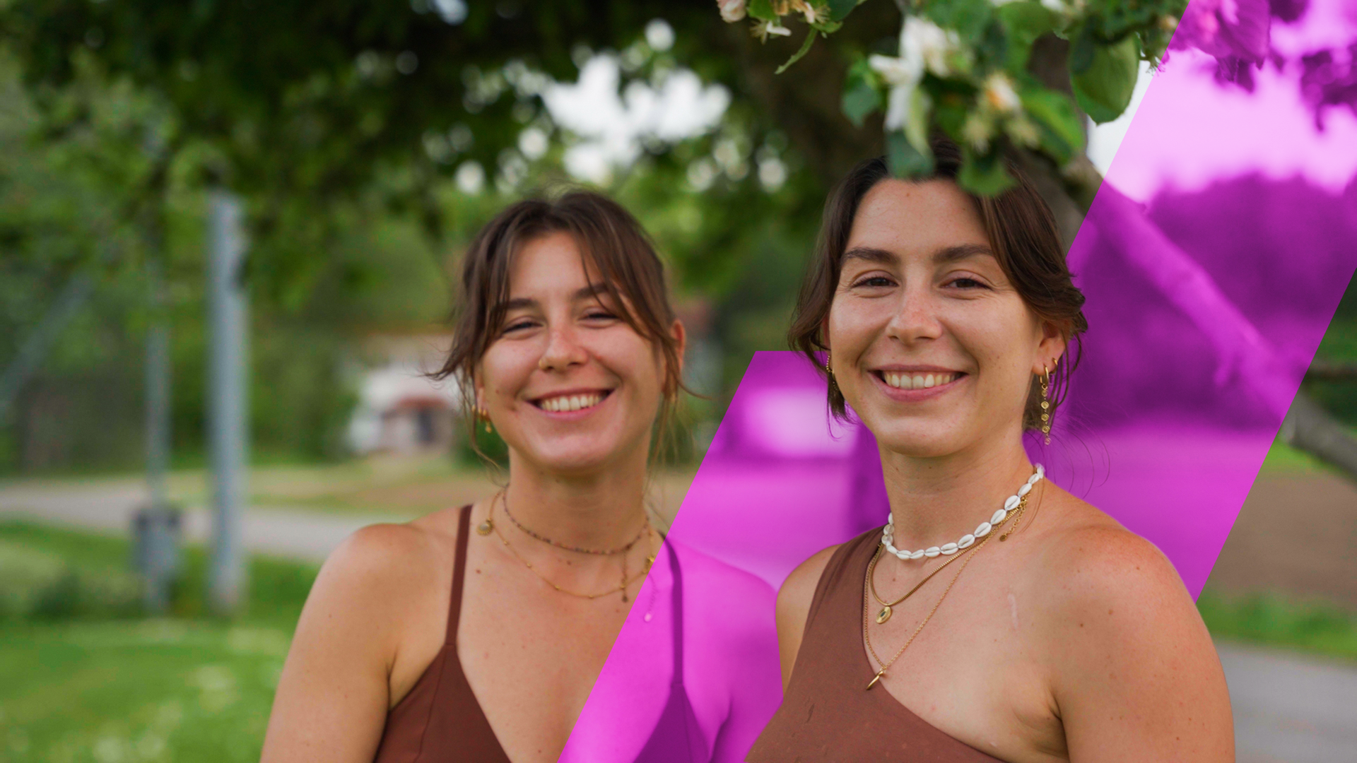 Julia und ihre Zwillingsschwester Eva stehen nebeneinander, Arm in Arm und lächeln in die Kamera. 