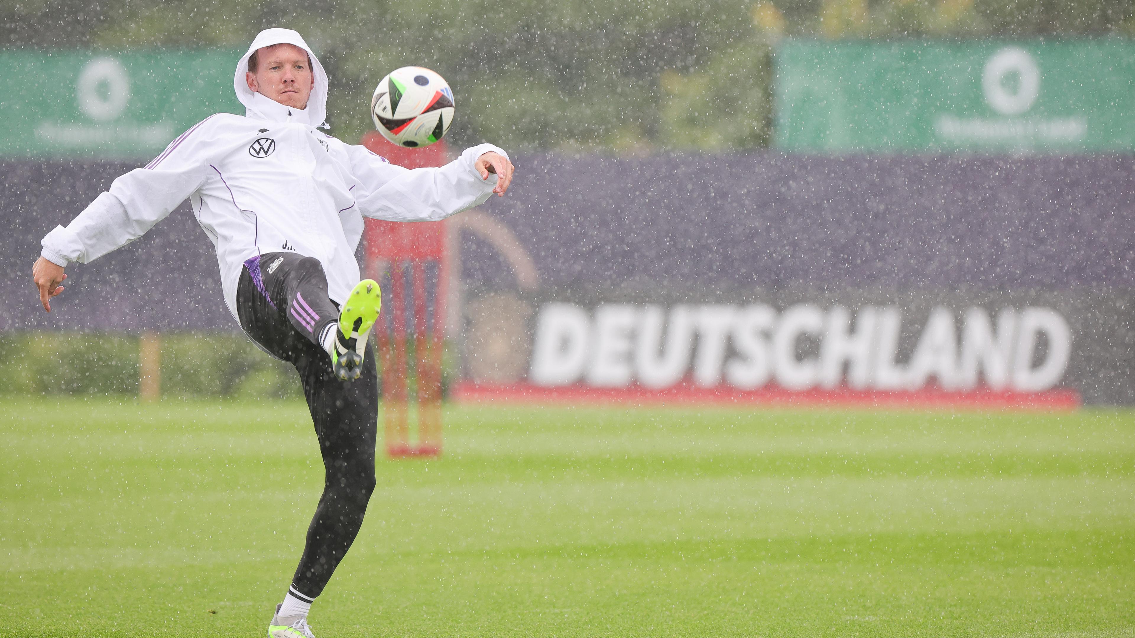Deutschlands Trainer Julian Nagelsmann spielt einen Ball zu Beginn des Trainings im strömenden Regen. 
