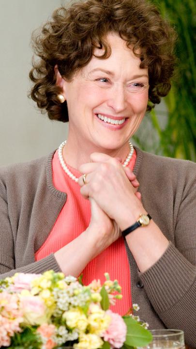 "Julie & Julia": Julia Child (Meryl Streep) sitzt freudestrahlend an einem mit blumen geschmückten Tisch.