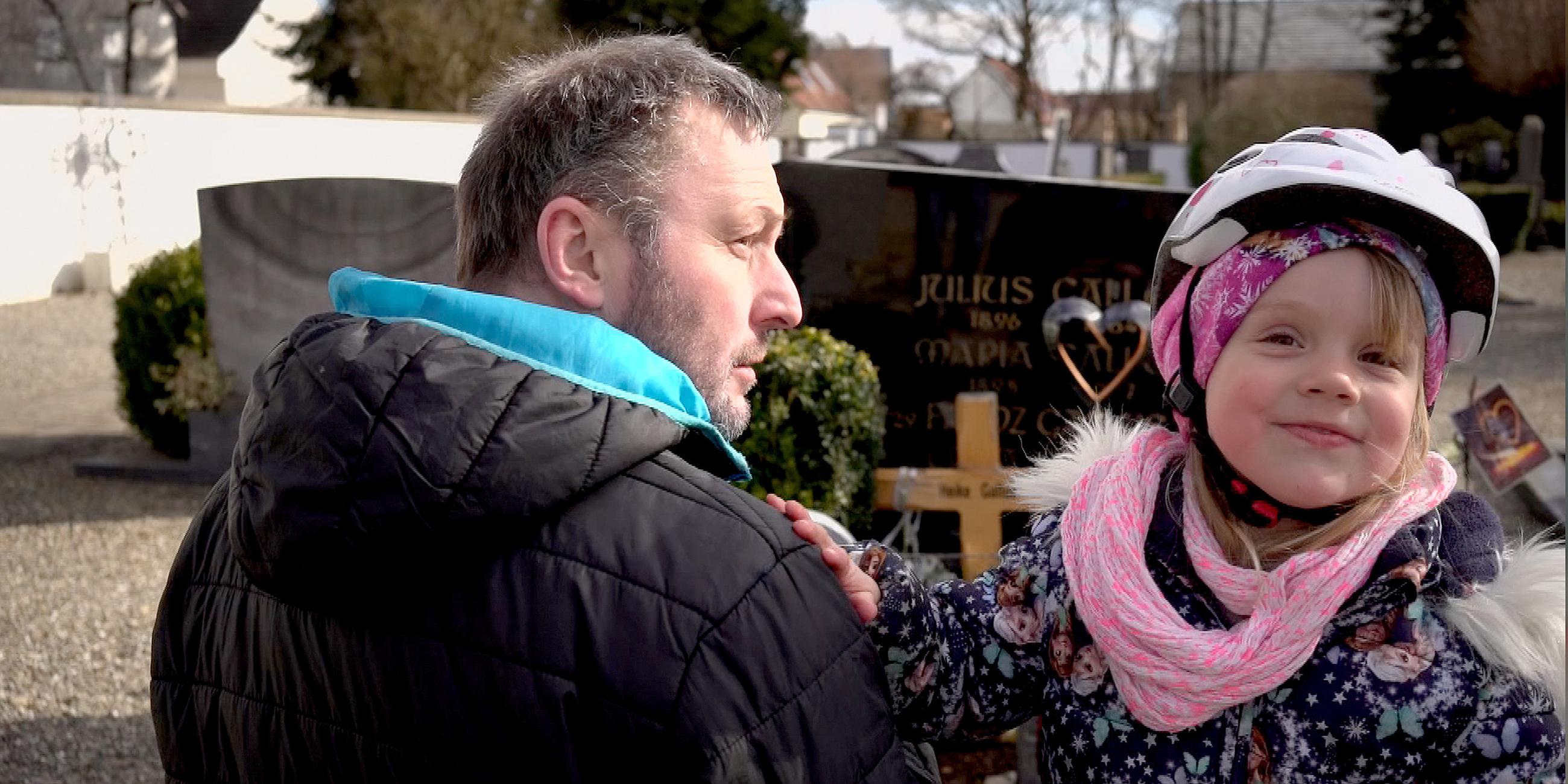 Stephan ist mit seiner dreijährigen Tochter Greta mit Fahrradhelm auf dem Friedhof.