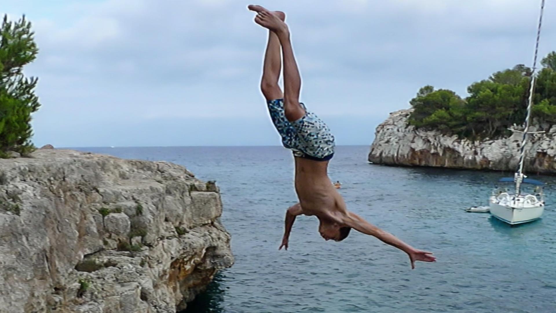 Ein Junge springt von einer Klippe ins Meer.
