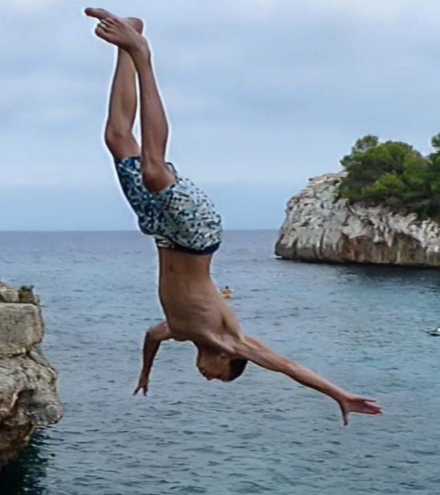 Ein Junge springt von einer Klippe ins Meer.