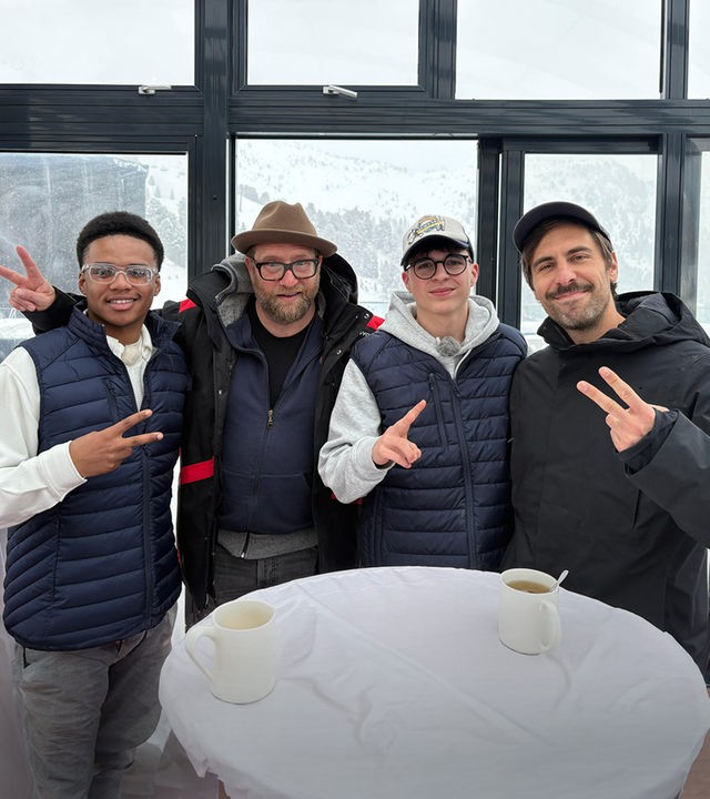 An einem Bistrotisch stehen zwei Jungs mit zwei Männern und grinsen in die Kamera. Alle machen das Victoryzeichen. Es handelt sich um Azad aus der Jungs-WG im Schnee, der neben dem deutschen Musiker Gregor Meyle steht. Daneben steht Nick und sein Idol, der Singer und Songwriter Max Giesinger. Im Hintergrund sieht man durch die großen Fensterscheiben schneebedeckte Berge.