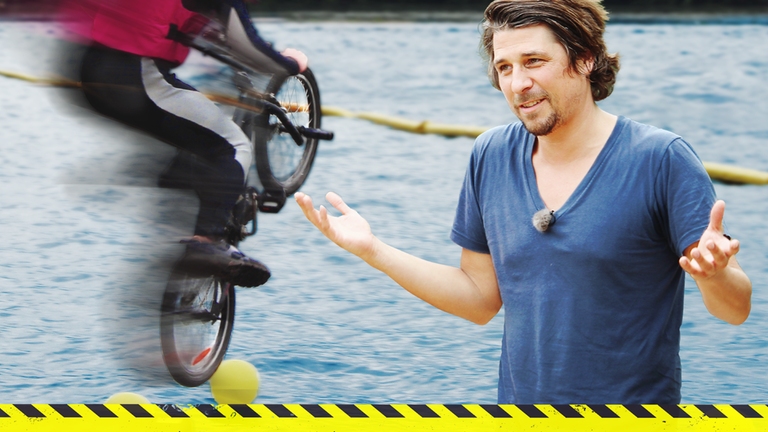 Tommy steht mit offenen Armen auf einer Halfpipe. Im Hintergrund sieht man einen Biker.