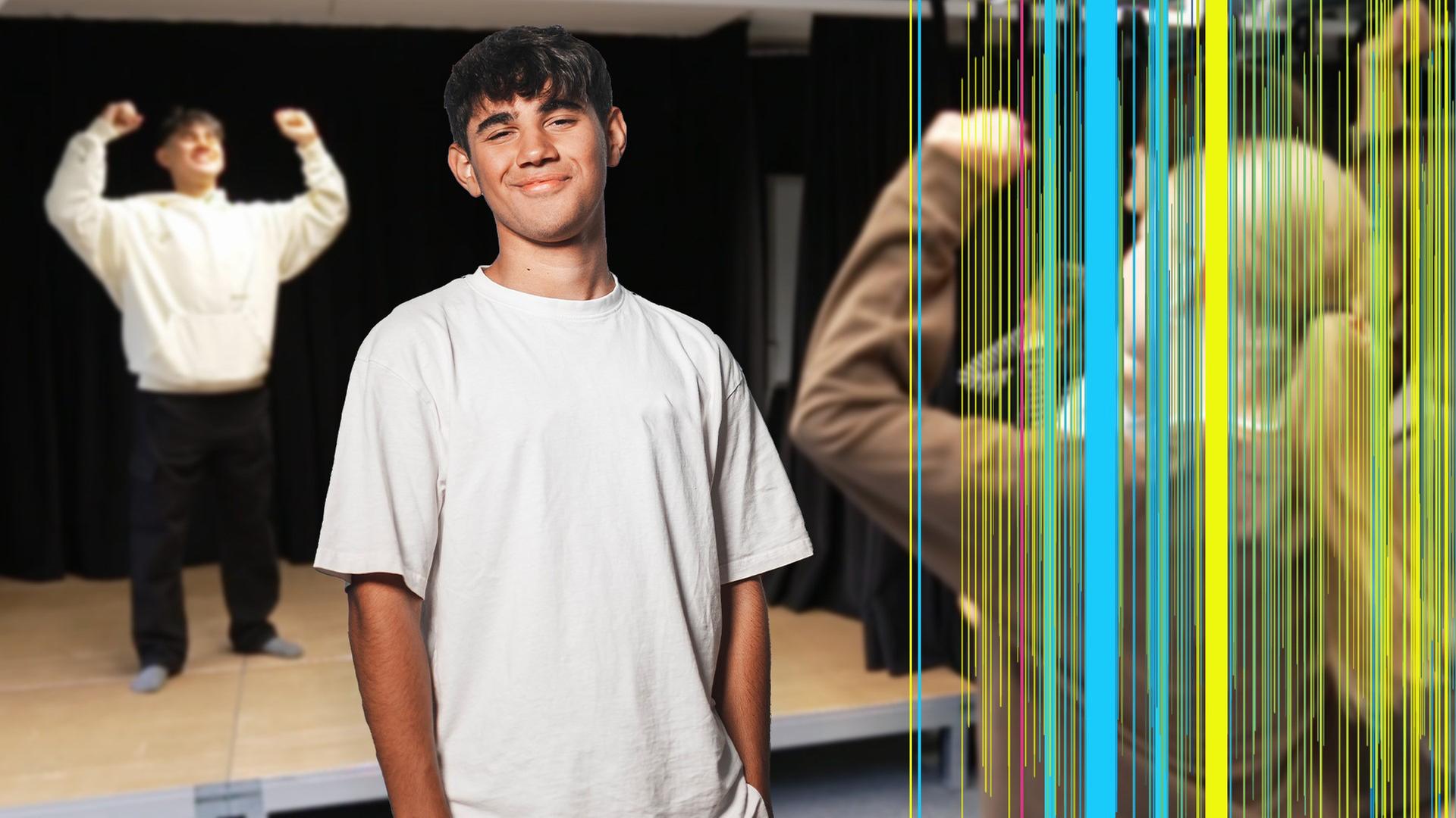 Ein lächelnder Junge ist in der Mitte des Bildes zu sehen. Er hat die Hände lässig in die Hosentaschen gesteckt. Im Hintergrund ist unscharf derselbe Junge in Siegerpose zu sehen, am rechten Bildrand ist unscharf eine Gruppe Mädchen zu sehen, die den Jungen offenbar fotografieren. 