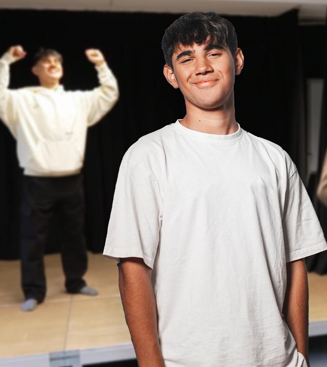 Ein lächelnder Junge ist in der Mitte des Bildes zu sehen. Er hat die Hände lässig in die Hosentaschen gesteckt. Im Hintergrund ist unscharf derselbe Junge in Siegerpose zu sehen, am rechten Bildrand ist unscharf eine Gruppe Mädchen zu sehen, die den Jungen offenbar fotografieren. 