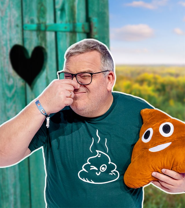 Elton steht vor einem Klo-Häuschen, hält sich die Nase zu und trägt ein Kack-Emoj-Kissen unter dem Arm. 